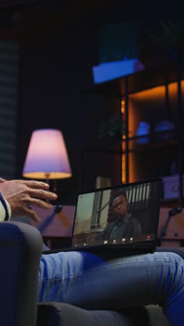 vertical video focused black guy smiling and waving during a web conference in his living room
