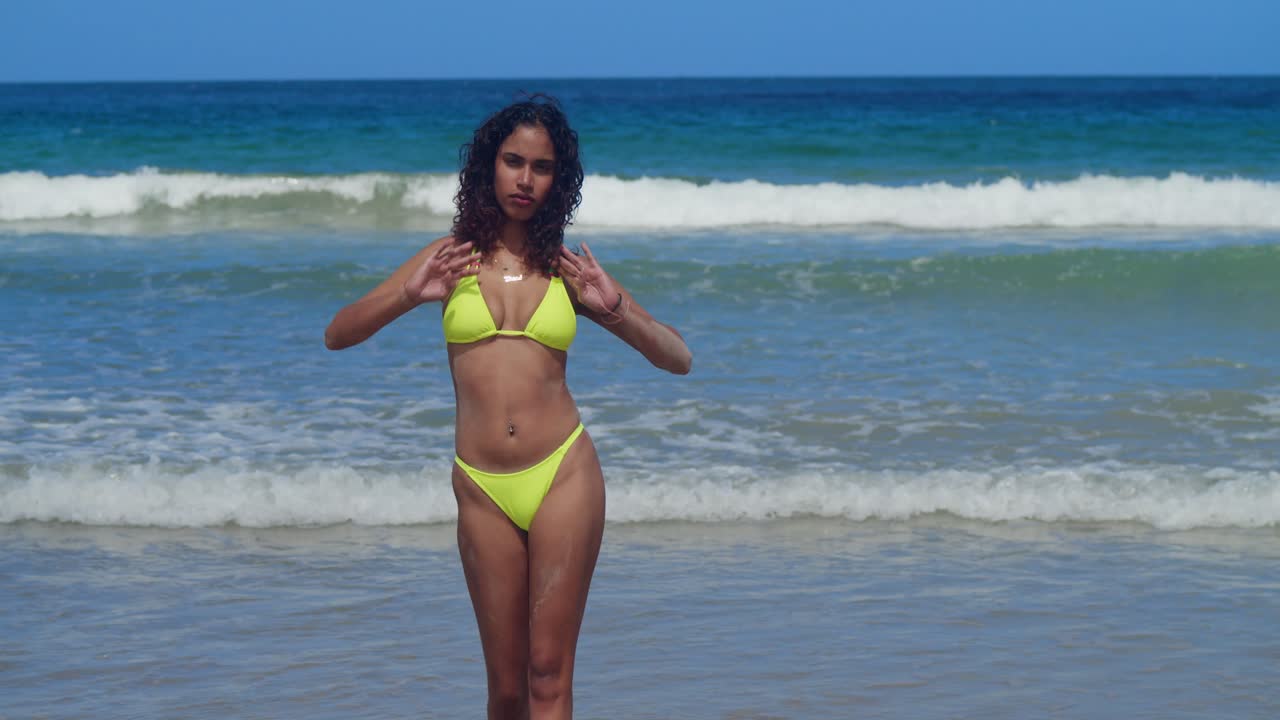 A young woman in a yellow two-piece swimsuit relaxes on a sunny, tropical Caribbean shore