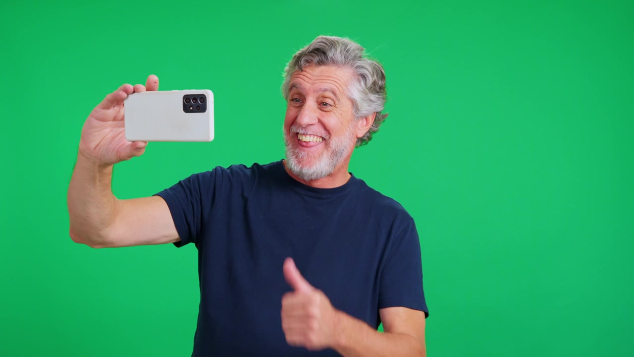 Senior man taking funny selfie with smartphone on green screen