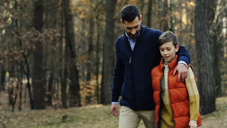 hombre caucásico caminando y hablando en el bosque con su pequeño hijo