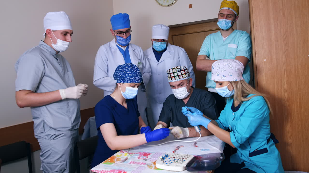 Blonde female student is putting a nozzle on the drill machine. A group of doctors watching the practice.