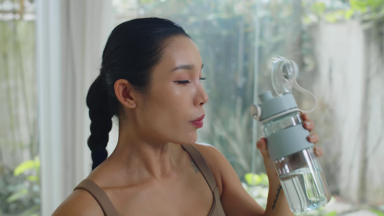 Tired Female Athlete Drinking Water after Training indoors