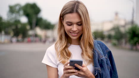 mujer joven feliz mirando el teléfono y caminando por la calle