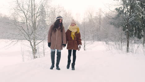 mother and daughter walk hand in hand in a snowy forest