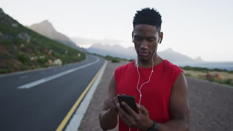 Hombre-Afroamericano-Usando-Auriculares-Usando-Un-Teléfono-Inteligente-En-La-Carretera