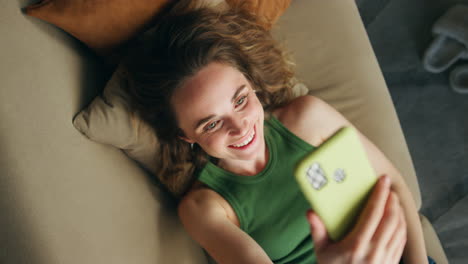 Niña-Feliz-Saludando-Con-La-Mano-Hablando-Con-La-Vista-Superior-Del-Teléfono-Inteligente.-Mujer-Relajada-Tendido-Sofá