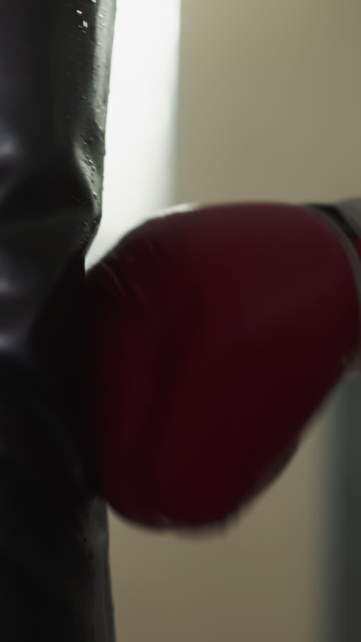 Robust man hand in glove delivers blow to combat bag showcasing strength. Enhanced endurance and physical wellbeing in gym. Building muscle via active movements