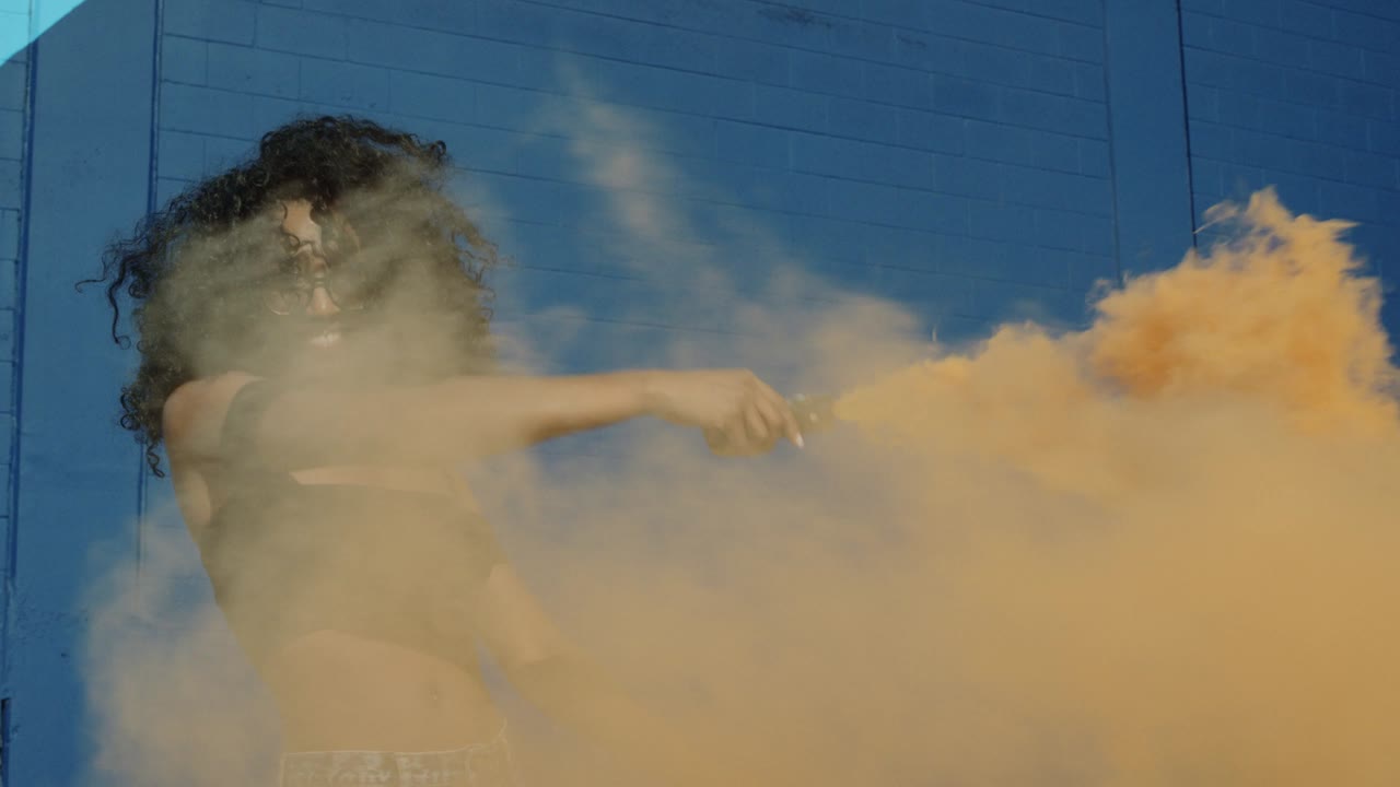 красивая молодая женщина с цветной дымовой гранатой танцует снаружи против синей стены