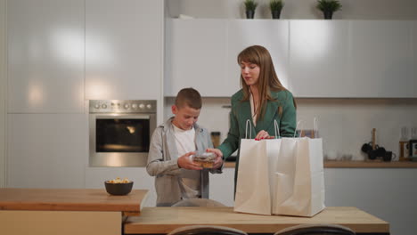 mother and son unpack shopping bags with food in kitchen