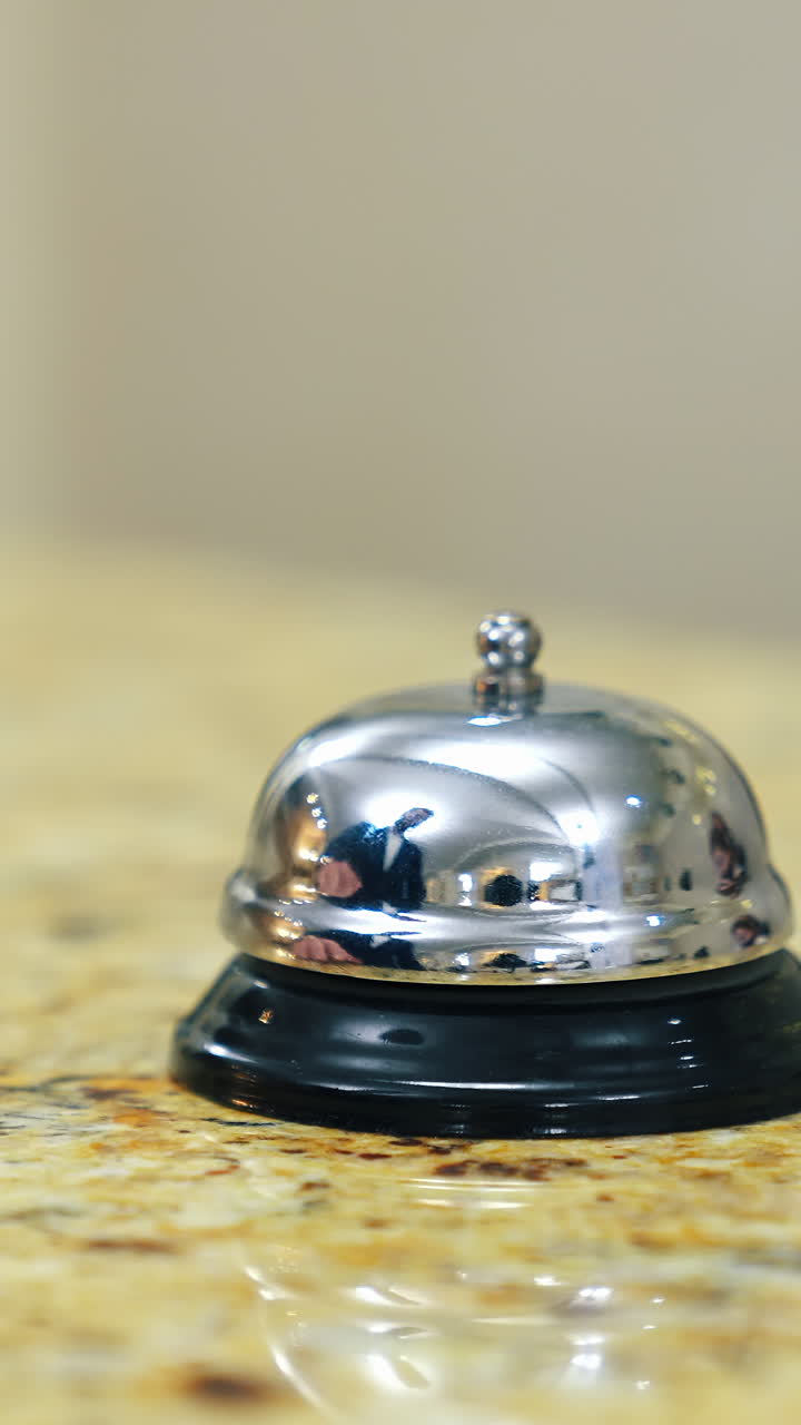 Hotel bell on reception table. Man's hand presses bell button to call the receptionist in the hotel. Customer touches the metal alarm. Close-up. Vertical video