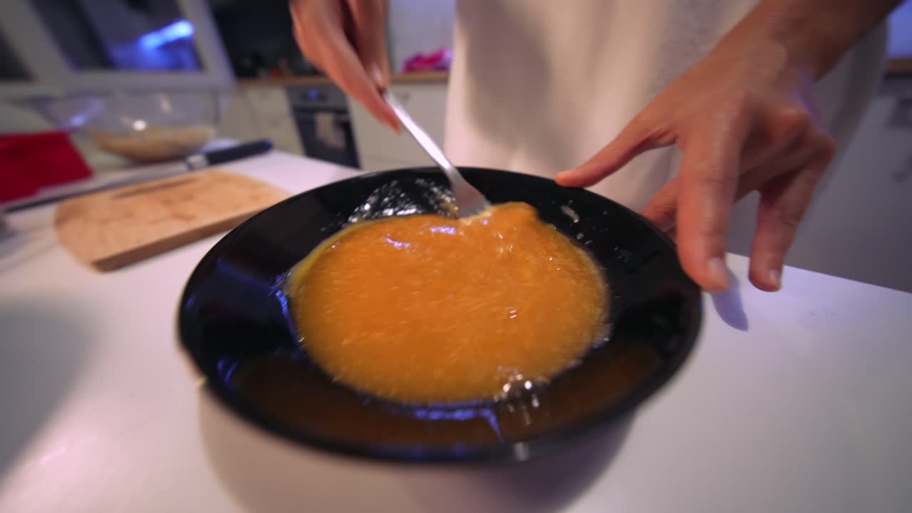 Primo piano di mani che mescolano uova in una ciotola nera con una forchetta
