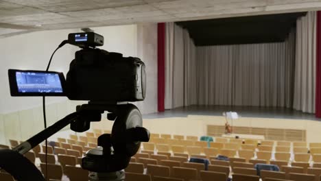 camera in an empty small concert steel with many chairs and empty stage on a tripod