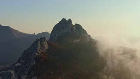 flying around the rocky top of the mountain where trees grow and the fog creeps in on an autumn alday on a sunny day