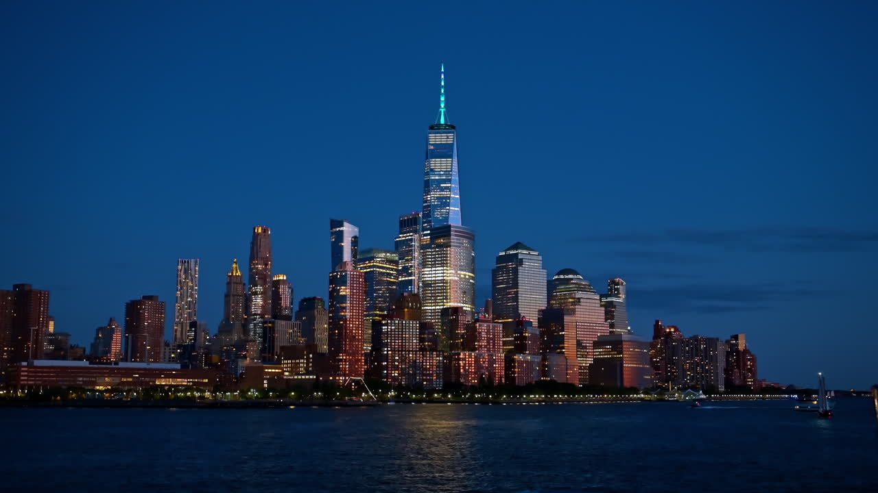 La guglia del One World Trade Center illuminata di notte. Vista dal basso della Freedom Tower e dello skyline di Lower Manhattan dall'altra parte del fiume.