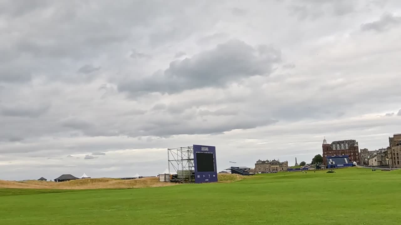 A scenic view of a green fairway with a distant clubhouse under a cloudy sky.