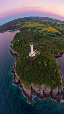 aerial view of a lighthouse on a lush coastal headland at sunset