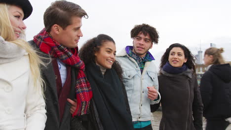 group of young friends walking over millennium bridge in london