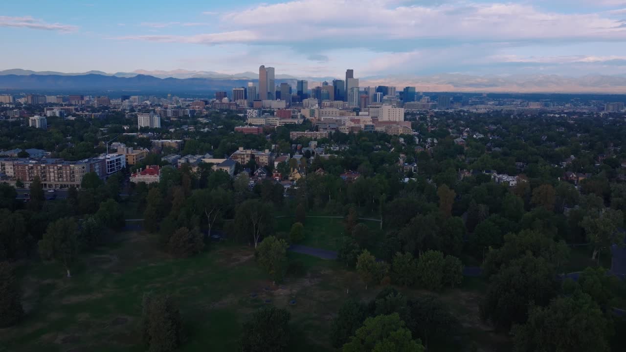 Panorama aereo della città di Denver con catena montuosa distante, dolce tilt up su un parco denso e alberi