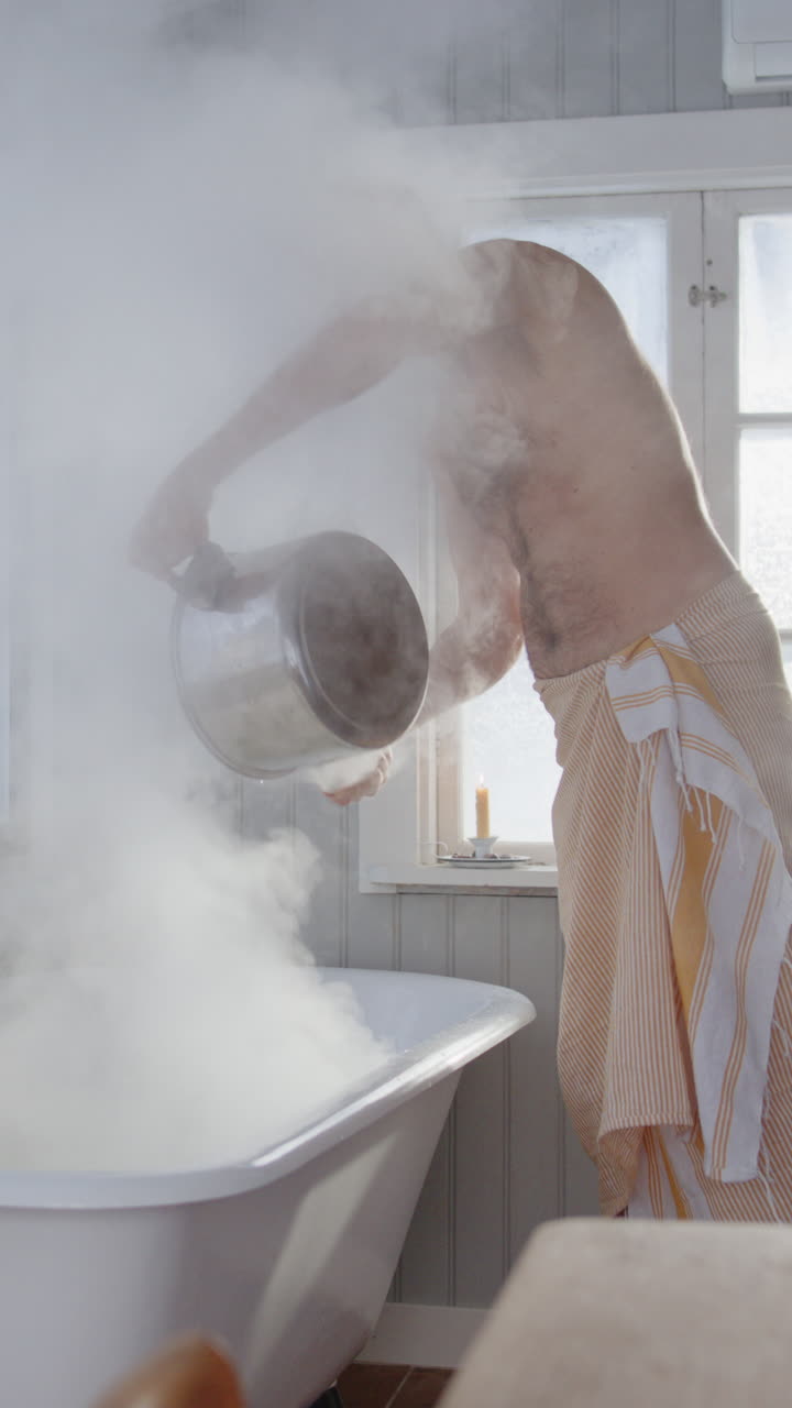 Bare chested man pour boiling hot water from woodstove into steam bath, vertical