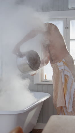 bare chested man pour boiling hot water from woodstove into steam bath, vertical