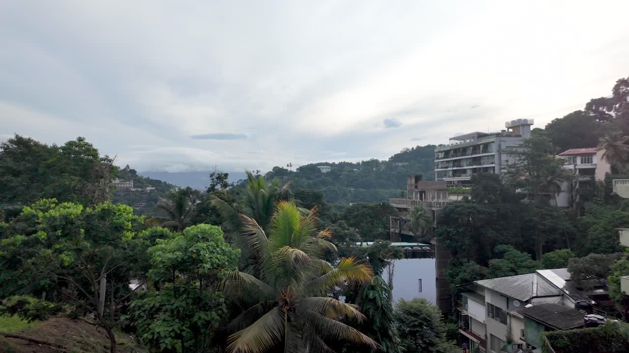 A scenic view over Kandy, Sri Lanka, showcasing lush trees and urban buildings. Pan Right Shot