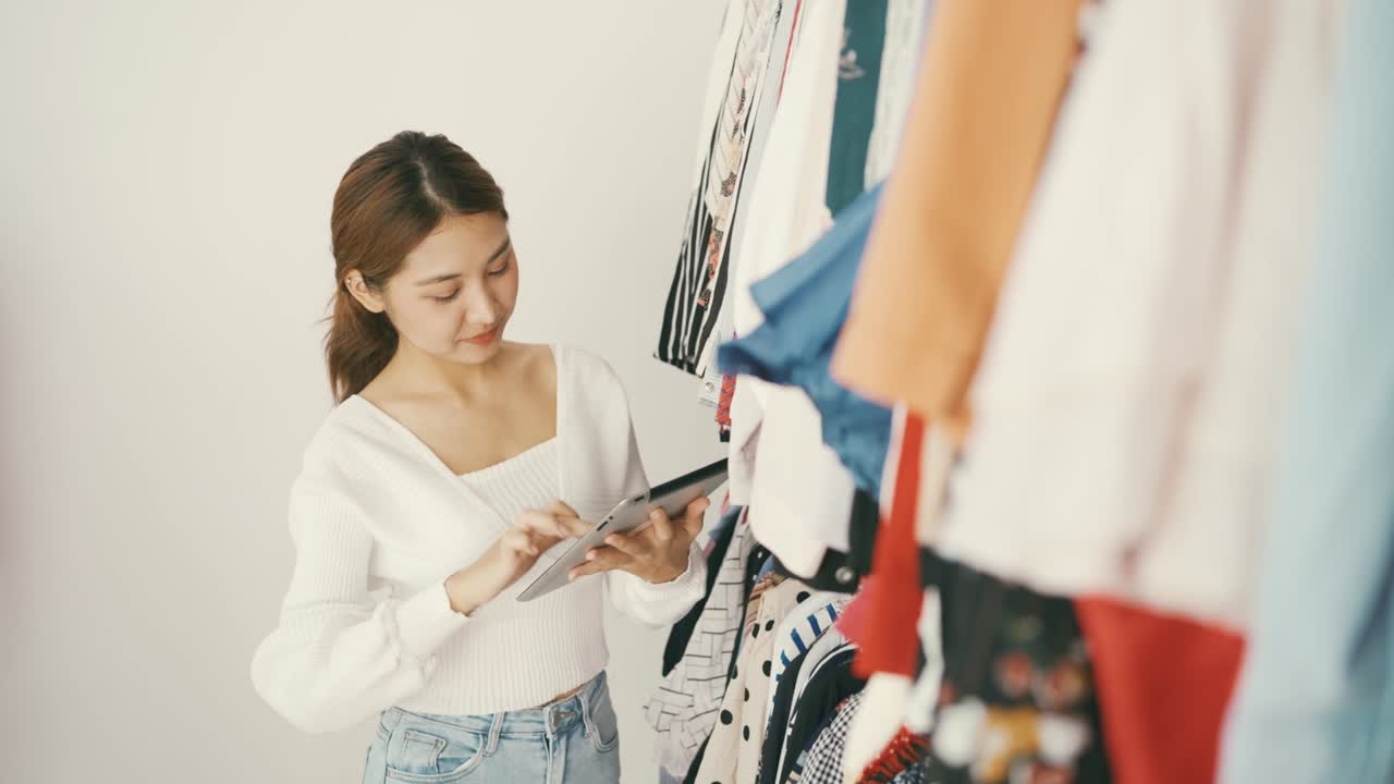 패션 상점의 기업가와 소규모 사업주들은 디지털 태블릿을 사용하여 의류 상점의 레일에 있는 재고를 확인합니다.