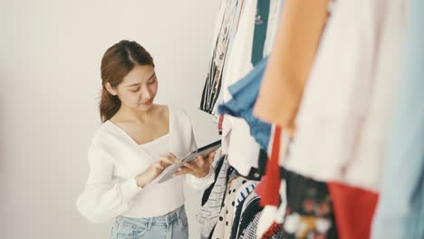 패션 상점의 기업가와 소규모 사업주들은 디지털 태블릿을 사용하여 의류 상점의 레일에 있는 재고를 확인합니다.