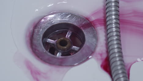 Dark-red-ink-rinsed-down-shower-drain,-close-up