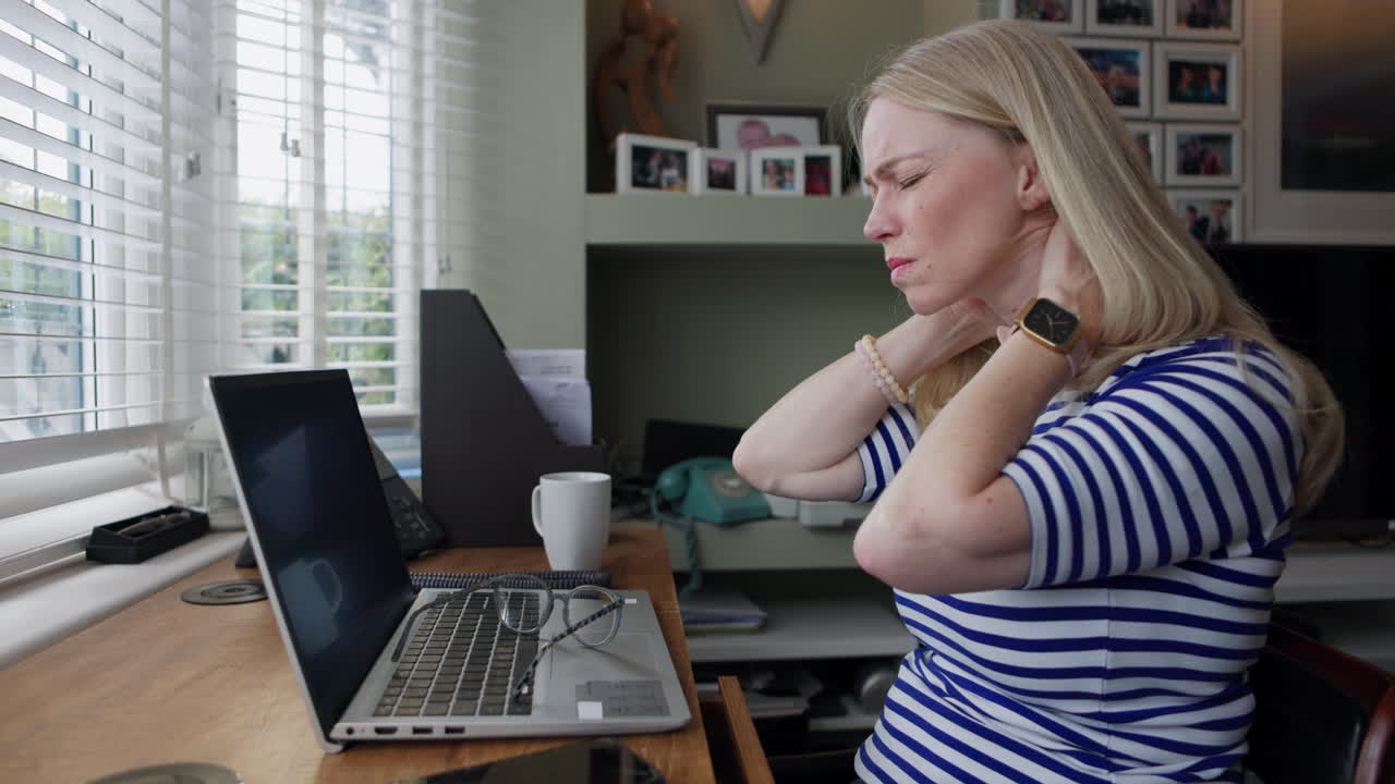 Woman experiencing neck pain while working at her computer in her home office