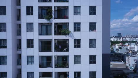 drone shot of high-rise modern residential building flying up to the top on sunny day looking into apartments, windows and balconies