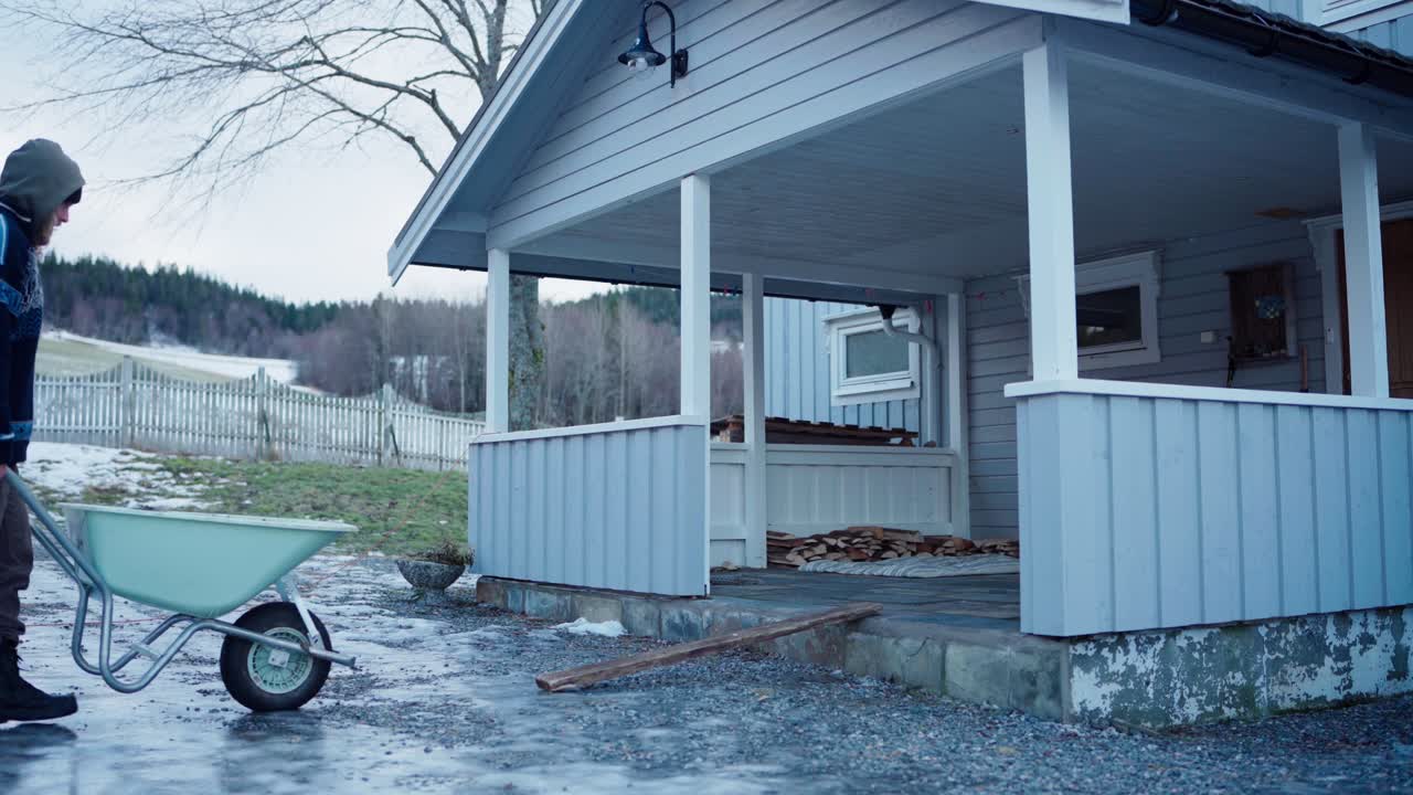 hombre empujando una carretilla cargada en una rampa de madera en la cabaña en invierno