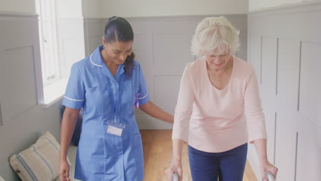 senior woman at home using walking frame being helped by female care worker in uniform