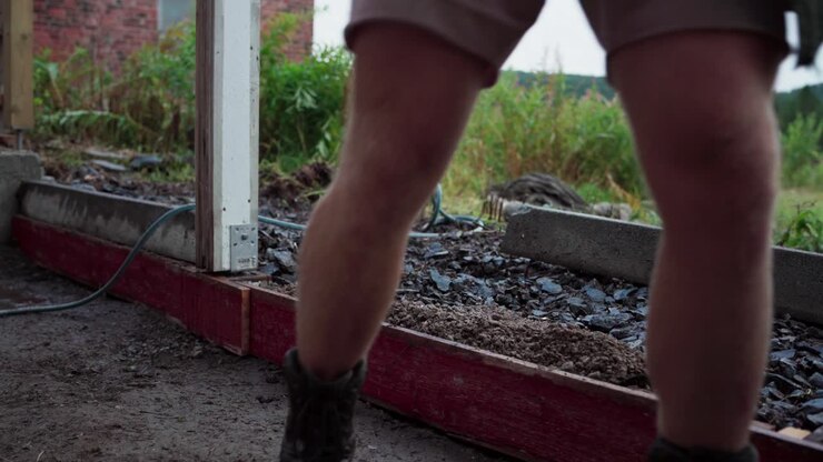 A Man is Utilizing a Shovel to Transfer and Subsequently Compact the Fill Soil During the Construction of a Greenhouse - Close Up