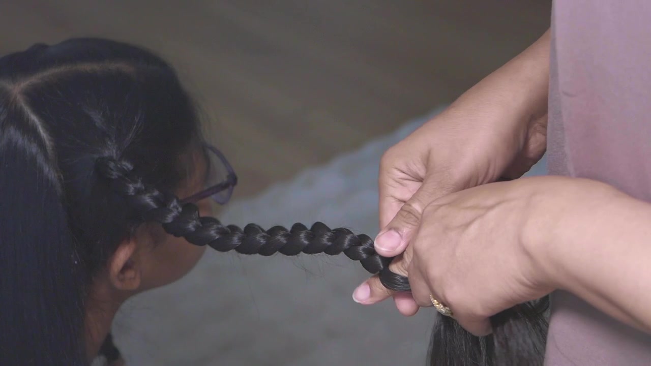 Primo piano di mani che intrecciano i lunghi capelli neri di un bambino