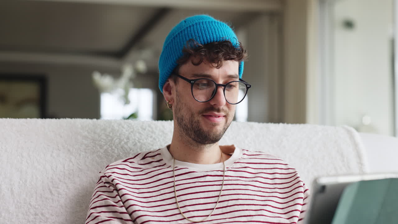 Man with blue beanie using tablet on couch