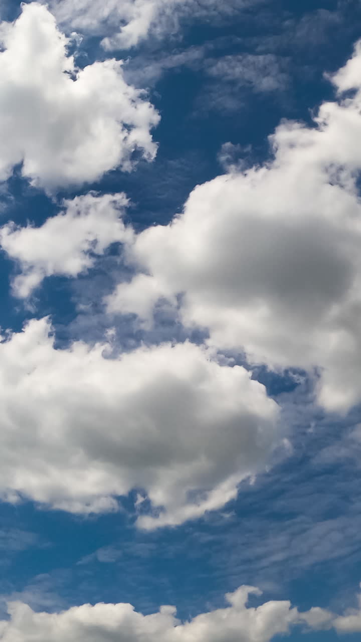 Diverse types of cloudscape in the atmosphere. Cumulus and stratus white clouds in the blue sky. Low angle view. Timelapse. Vertical video