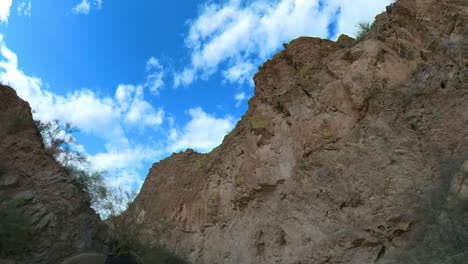 Hiker-walks-towards-a-rocky-cliff-face-towering-over-a-sandy-wash