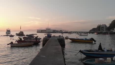 una aproximación aérea a baja altura sobre un muelle ubicado en un pueblo frente al mar ubicado en una bahía rodeada de barcos, árboles y naturaleza