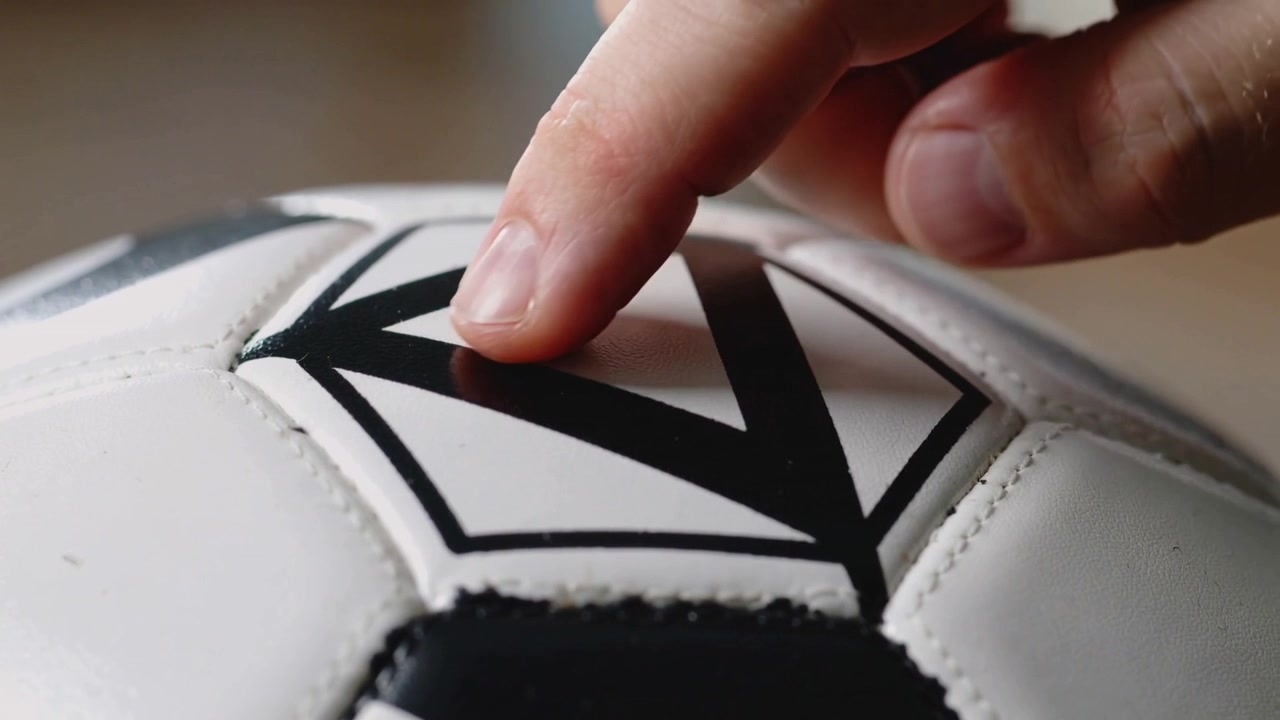 Ponta do dedo tocando, pressionando e deslizando em uma bola de futebol costurada sobre a mesa, exibindo um decalque.