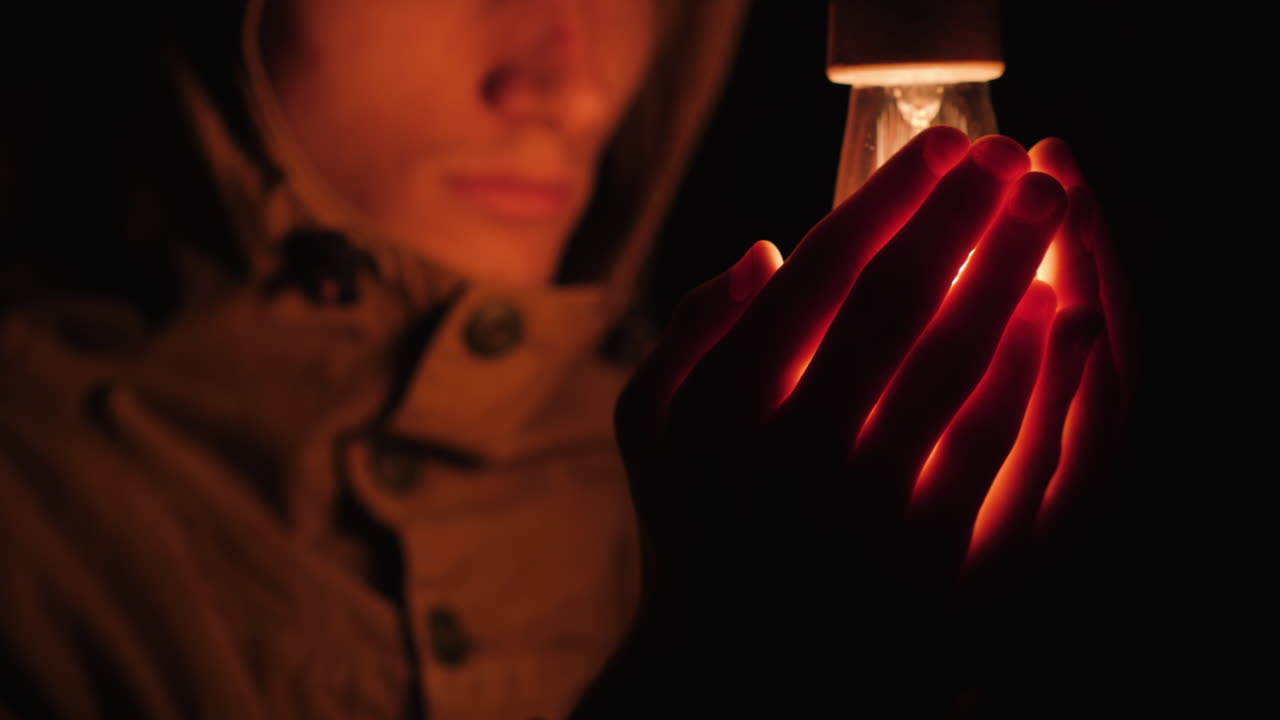hombre triste calienta sus manos cerca de una bombilla en la oscuridad