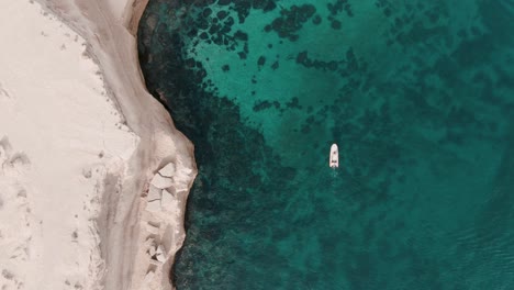 boat moving next to a cliff in shalow clear waters in patagonia from a drone top shot slowmotion