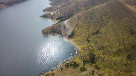 Aerial-view-of-terraced-farm-fields-and-boats-docked-along-the-shore-of-Lake-Titicaca,-Bolivia