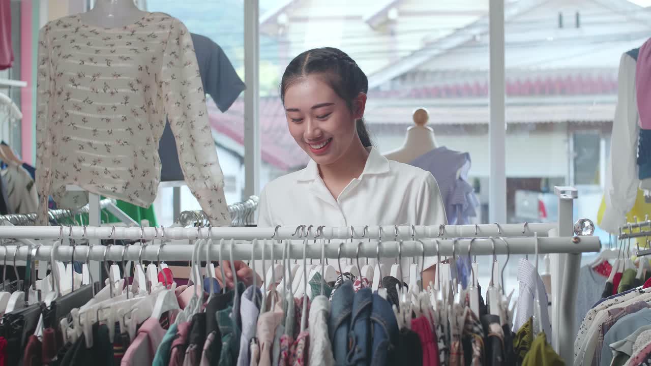 젊은 아시아 여성 은 부티크 에서 쇼핑 하는 동안 거 에 있는 옷 을 선택 하는 것 을 즐긴다