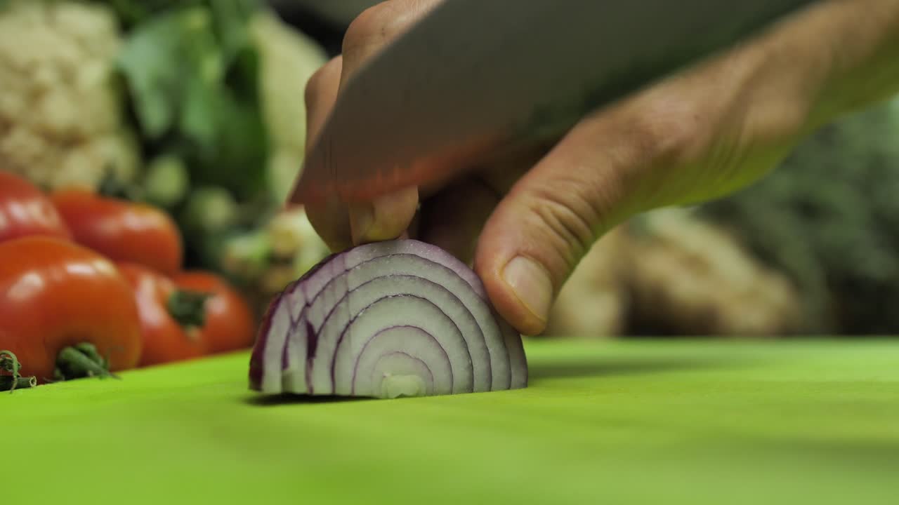 Chef slice red onion on cutting board on fresh vegetable background, close up
