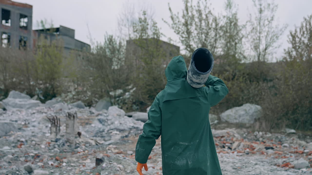 Survivor after nuclear chemical war. Man in safety clothes carrying pipe in abandoned polluted place on ruined buildings background.