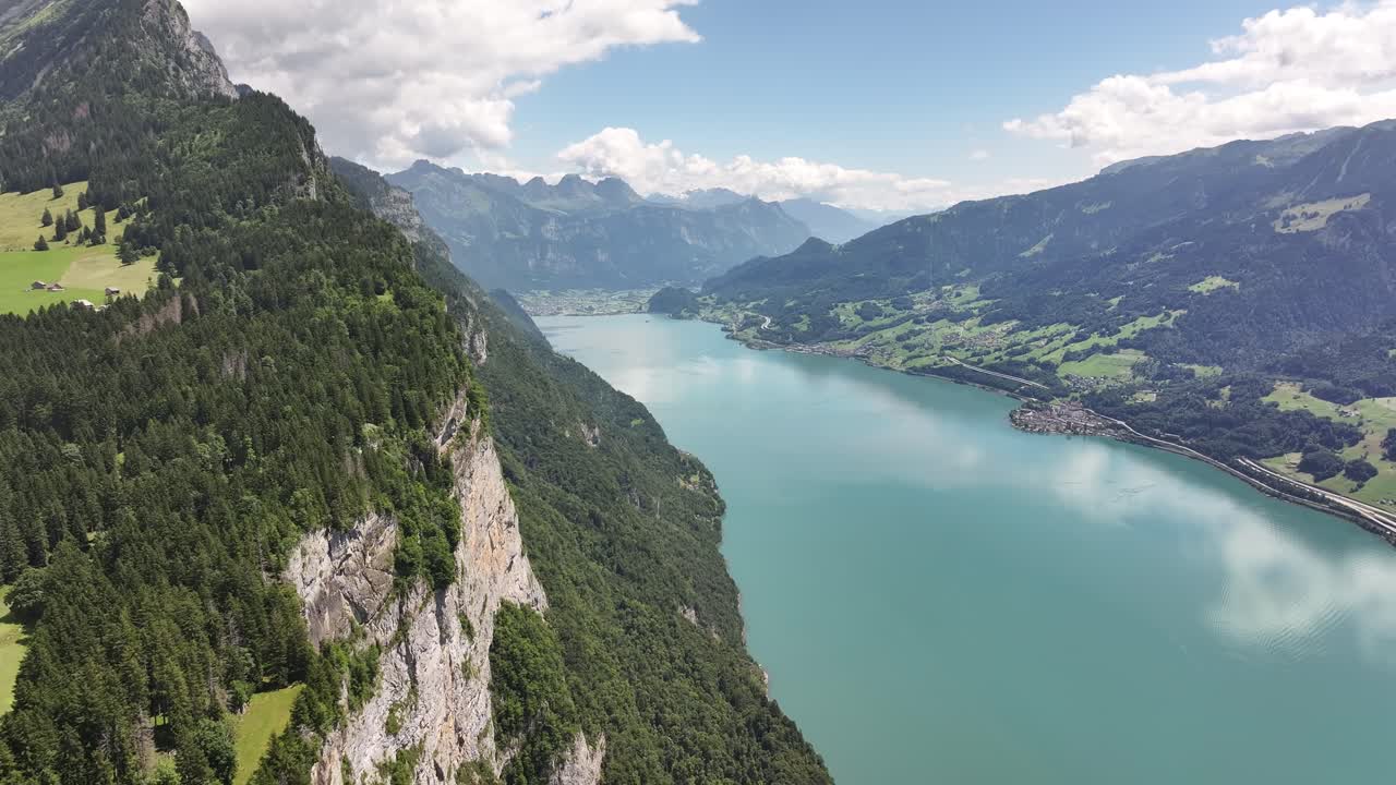 Aerial view reveals the majestic, turquoise waters of Walensee, Switzerland, flanked by lush green, steep mountains. The village of Weesen is visible on the lake's shore, nestled in the valley