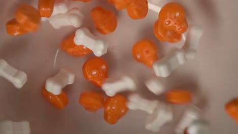 Extreme-closeup-of-orange-skulls-and-bones-shaped-candy-falling-on-a-plate