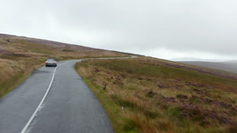 Forwards-fly-above-road-in-countryside-on-cloudy-day.-Following-vintage-convertible-car-with-textile-roof.-Ireland
