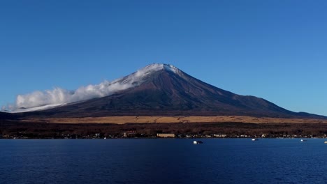 snow-capped mount fuji looms over lake kawaguchi, clouds gently drifting by, in a serene daytime scene