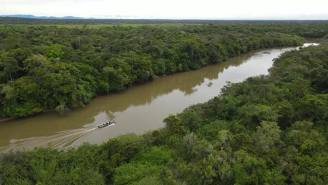 cinematic aerial view, boat sailing in muddy river deep in south american jungle